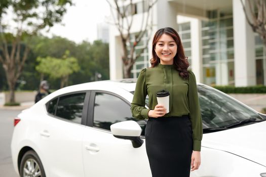 Portrait of smiling sexy woman drinking mug of beverage while standing near car outside