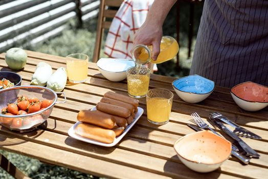 Young man preaparing table for picnic , holding bottle with lemonade in sunny summer afternoon. Backyard barbecue