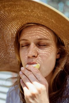 Headshot of woman in straw summer hat eating grilled vegetables outdoors, eyes closed. Light and shadow pattern on the face