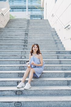 Beautiful young Asian woman sitting at outdoor stair and using smartphone. Lifestyle of modern female.