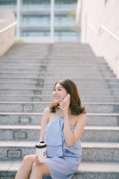 Cheerful young Asian girl talking on phone while sitting at outdoor stair. Lifestyle of urban girl.