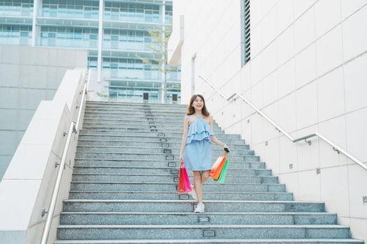 Portrait of young Asian woman going down stairs with color shopping bag. Lifestyle and shopping concept.