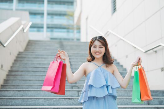 Happy Asian woman going down stairs with many colorful shopping bags. Lifestyle and shopping concept.