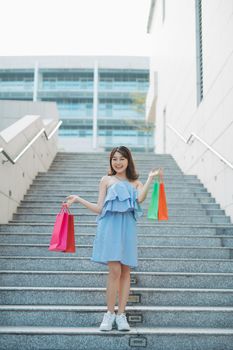 Portrait of young Asian woman going down stairs with color shopping bag. Lifestyle and shopping concept.