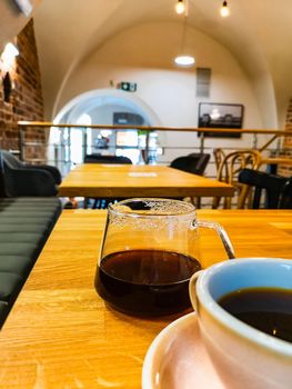 Drinking black coffee from white cup and glass jug in small cafe