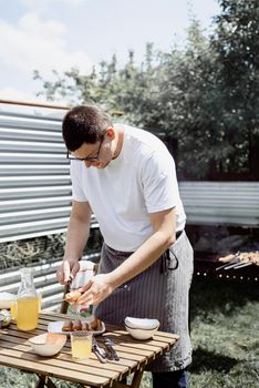 Backyard barbecue. Mans hands grilling kebab and vegetables on metal skewers.