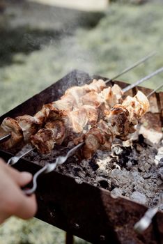 Backyard barbecue. Mans hands grilling kebab and vegetables on metal skewers.