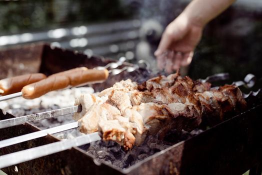 Backyard barbecue. Mans hands grilling kebab and vegetables on metal skewers.