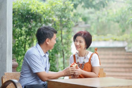 Asian middle-aged man gives a present to his wife in anniversary wedding day