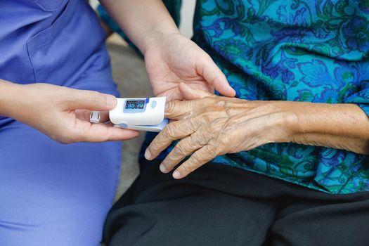 Caregiver monitoring oxygen saturation at fingertip of elderly woman.