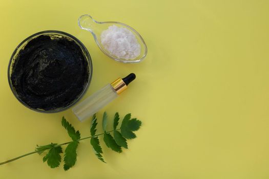 Image of the ingredients of home cosmetics. Black mask, black dirt, pink salt, a bottle with an eyedropper on a yellow background.Skin Care Concept.