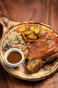 SCHWEINSHAXE traditional german pork knuckle with sauerkraut and potatoes bavarian meal on rustic wood background