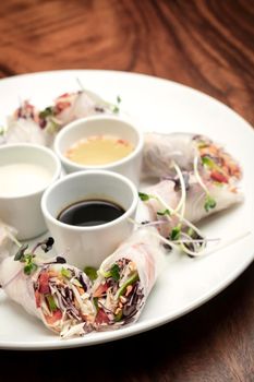 asian fresh vegetable vegan spring rolls with sauces on wood restaurant table background in vietnam
