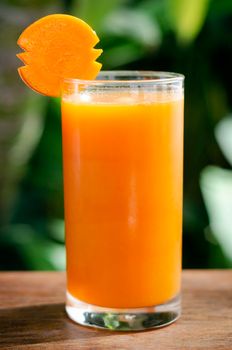 glass of fresh organic carrot juice on table outdoors on table in sunny garden outdoors