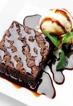 vegan chocolate brownie dessert with dairy-free coconut milk vanilla ice cream with caramel sauce on white background in studio