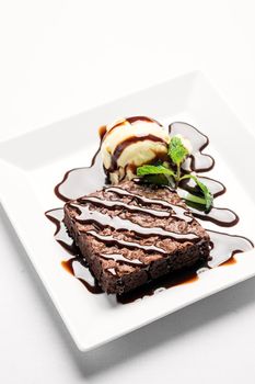 vegan chocolate brownie dessert with dairy-free coconut milk vanilla ice cream with caramel sauce on white background in studio