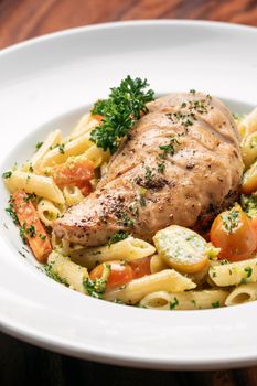 fried chicken breast with penne and saute vegetables pasta dish on wood table background