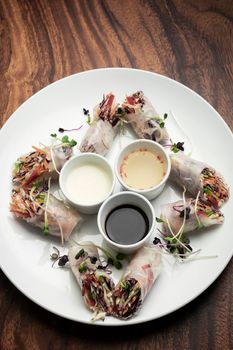 asian fresh vegetable vegan spring rolls with sauces on wood restaurant table background in vietnam