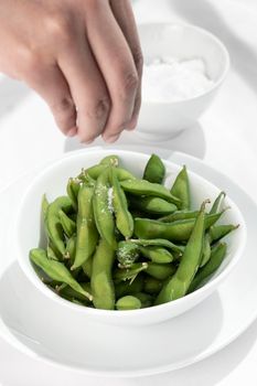 hand salting edamame beans snack in bowl on white restaurant table