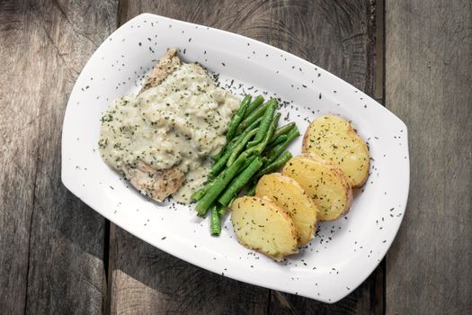 chicken breast with blue cheese sauce and roast potatoes with green beans on rustic old wood background