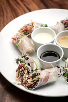 asian fresh vegetable vegan spring rolls with sauces on wood restaurant table background in vietnam