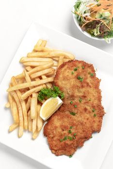 german breaded pork schnitzel with french fries on white studio background