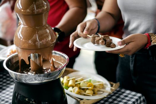 chocolate fountain catering machine with fruit skewers on rustic buffet table