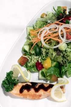 organic mixed vegetable salad with salmon fillet and balsamic vinaigrette on white restaurant table