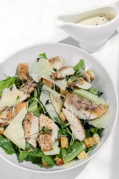 organic chicken caesar salad with parmesan cheese and croutons on white table background