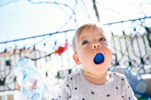 Small child stuffed a plastic bottle cap into his mouth, which he is holding in his hand. High quality photo