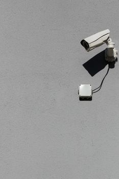 small white surveillance camera on flat gray matte plaster wall pointing sideways