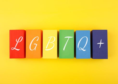 Flat lay with lgbtq plus text written on colorful rectangular geometric figures on yellow background. Concept of Pride Month, equal rights, LGBT community, respect and tolerance. 