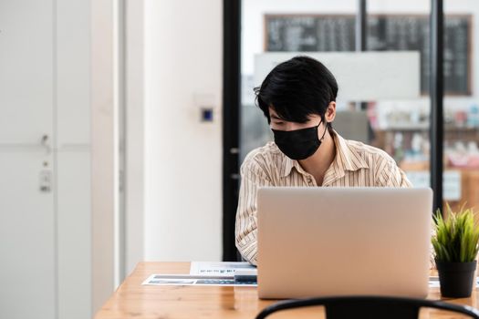 Young male employee wearing a health mask Preventing corona virus infection covid-19, concept of working from home and social distancing.