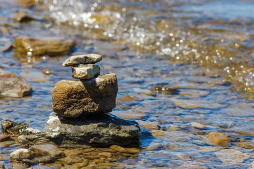 Stones are balanced and stacked on top of each other in the shallow water of a rocky beach at the edge of a river.