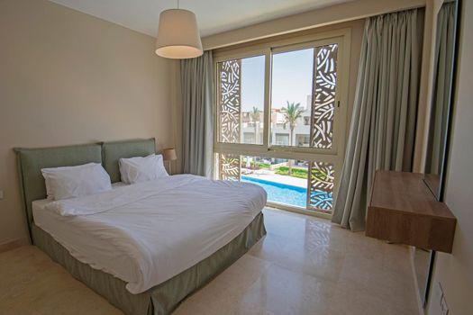 Interior design decor furnishing of luxury show home bedroom showing furniture and double bed in resort with swimming pool view