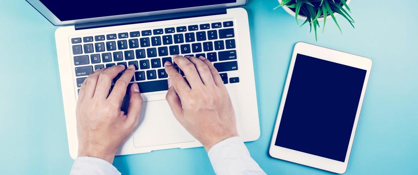 Hand of businessman working on laptop computer with plant and tablet and phone on desk in office, hand typing keyboard on notebook and workplace with copy space, top view, flat lay, business concept.