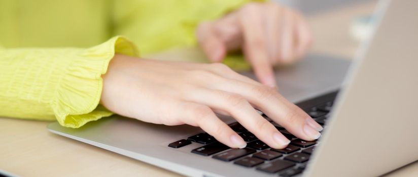 Closeup of hand young asian businesswoman working on laptop computer on desk at home office, freelance looking and typing on notebook on table, woman studying online, business and education concept.