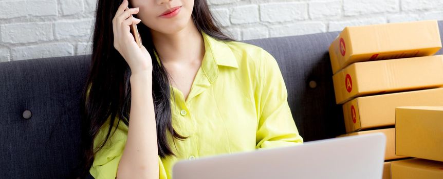 Young asian woman is entrepreneur talking with customer and using laptop computer while order purchase online at home, logistic and delivery, online shopping, female is seller of business SME.