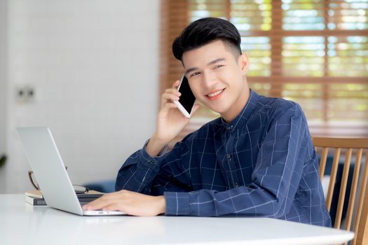 Young asian man talking phone and work from home with laptop computer, freelance using notebook to internet online and speak on smartphone, domestic life, business and communication concept.