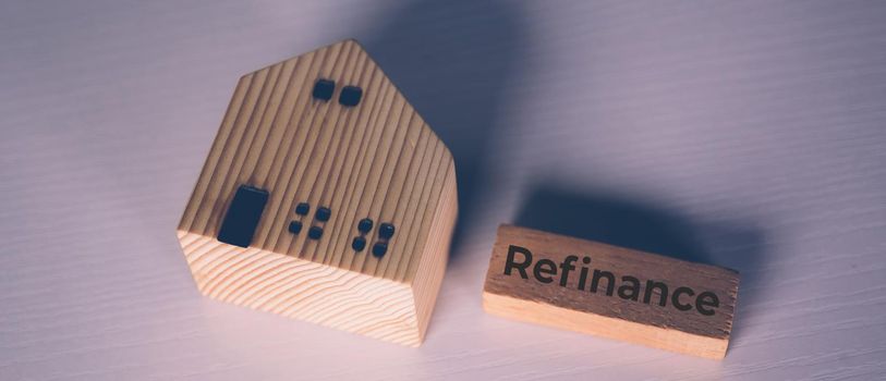 Wooden block with refinance word and house model about home and finance, loan and mortgage for real estate and property, residential and planning with budget, investment and earning, business concept.