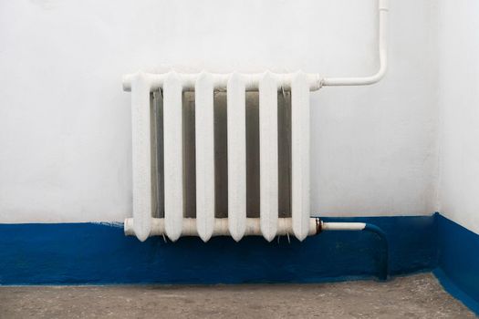 Old white radiator near the old dirty wall with dusty floor.