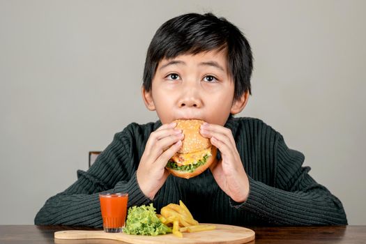 Cute Asian boy eating a delicious hamburger with happiness