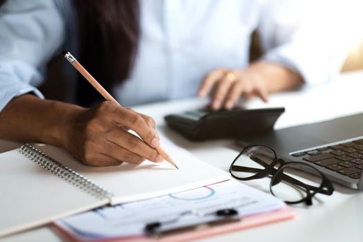 Close up of businessman or accountant hand holding pen working on calculator and laptop computer to calculate business data during make note at notepad, accountancy document at office.