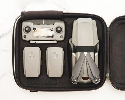 Folding drone quadcopter with full set in case. Top view or flat lay. Kit of drone UAV and accessories - controller and two battary in case over white marble background