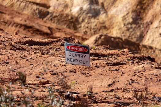 Photograph of a keep out safety danger sign on a barbed wire fence in a large quarry