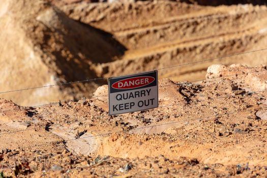 Photograph of a keep out safety danger sign on a barbed wire fence in a large quarry