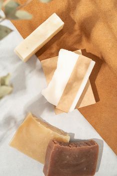 Natural organic cosmetics. Top view of handmade soap with craft blank band on double textured leather background with eucalyptus shadow