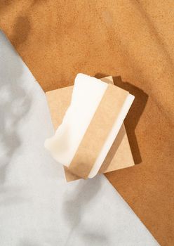 Natural organic cosmetics. Top view of handmade soap with craft blank band on double textured leather background with eucalyptus shadow
