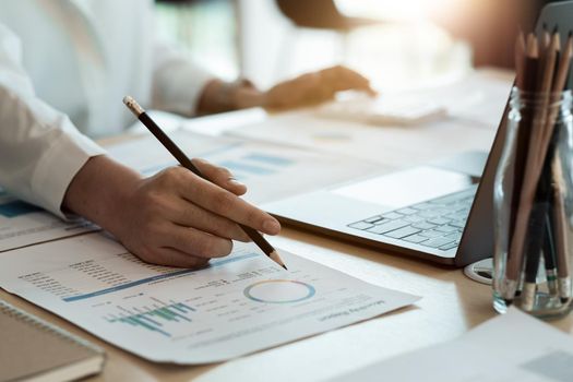 Close up of businesswoman or accountant hand holding pen working on calculator to calculate business data, accountancy document and laptop computer at office, business concept.