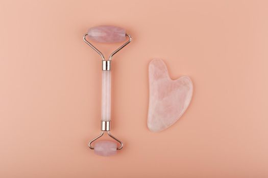 Jade roller and heart shaped guasha scraper massager made of pink quartz on pastel beige background. Concept of self treatment and facial guasha massage for skin lifting and toning